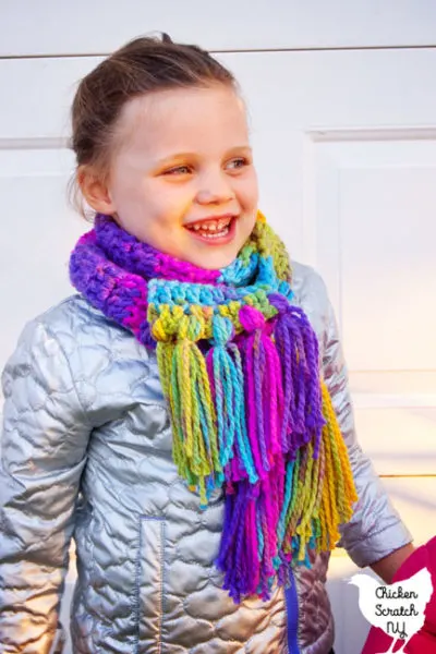 4 year old girl in silver coat wearing a rainbow colored hand crocheted scarf made with charisma yarn