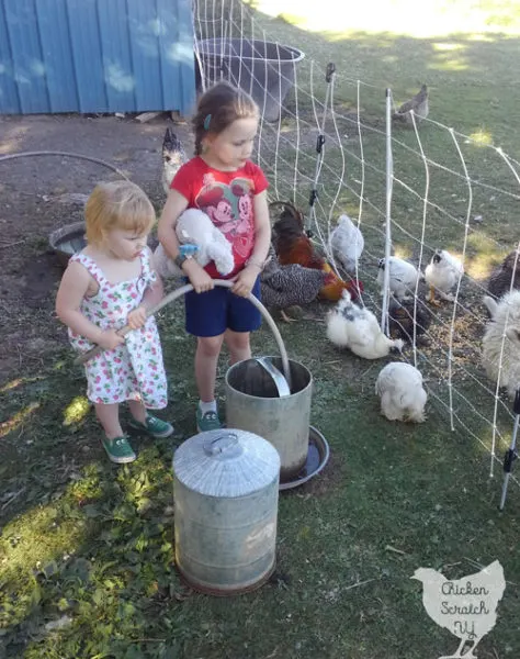 two little girls filling chicken wateres with a hose surrounded by chickens