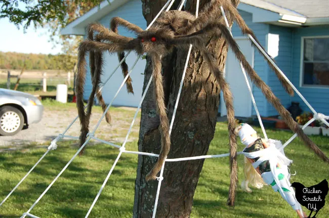 close up of halloween diy spider web decoration with large brown spider and barbie tied up with white fabric