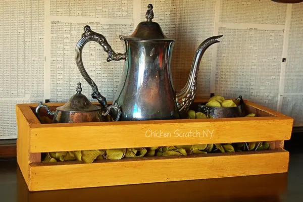 mustard yellow crate with wax finish holding metal teapot and sugar bowls in front of newspaper print walls