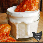 chicken wing with mango sriracha sauce in small small mason jar filled with white sour cream sauce