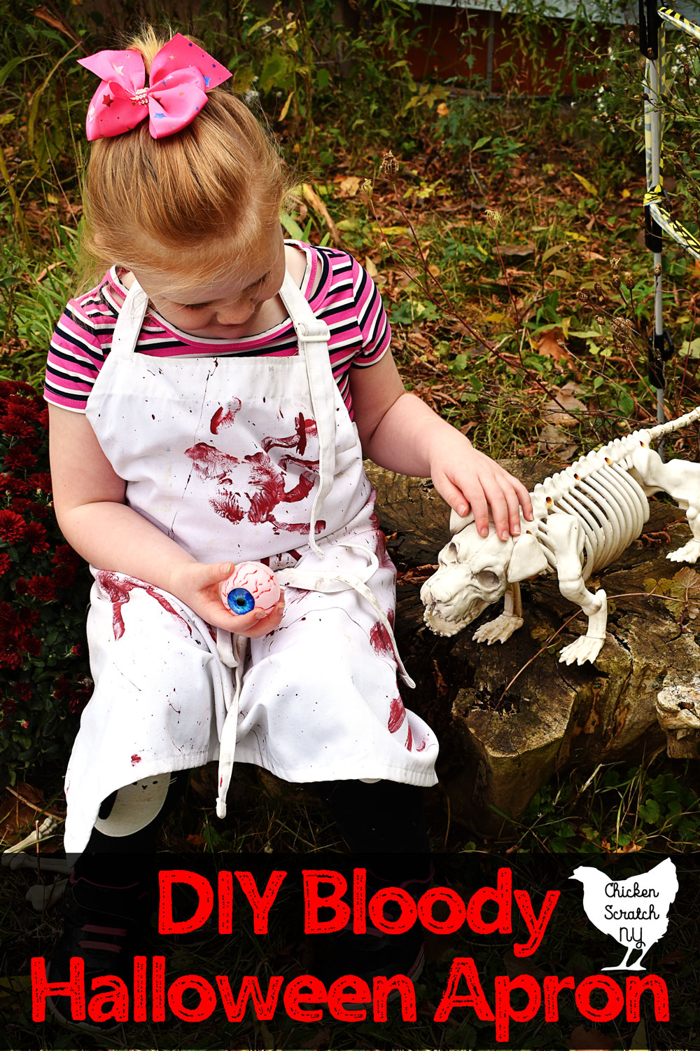 little blonde girl sitting on a stump wearing a white apron covered with red bloody hand prints holding an eyeball and petting a skeleton dog