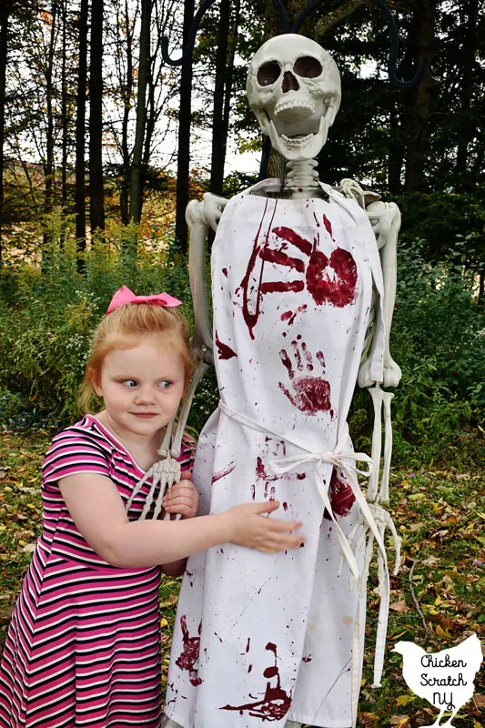 little blonde gold holding hands with a skelton wearing a bloody Halloween apron