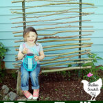 little girl sitting infront of homemade trellis made with branches, zip ties and t-posts