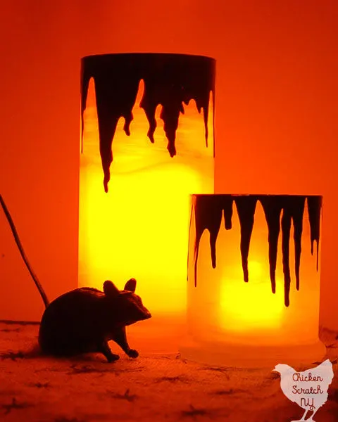 two candles holders light up with dark red drips that loop like blood on a spider sprinted burlap table cloth with a plastic rat
