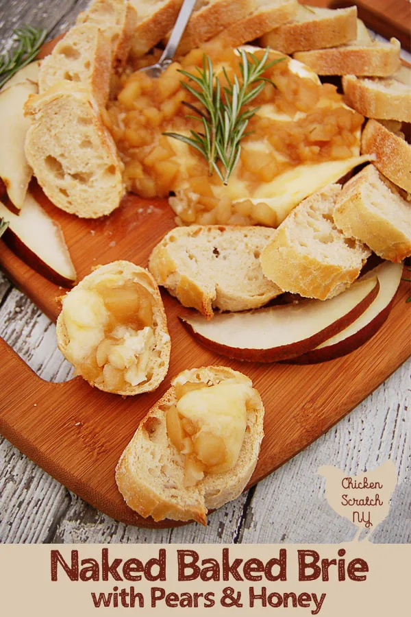 wooden cutting board sitting on white weathered wood surface with a baked brie covered in pear composte made with pears, honey and rosemany with slices of toasted crusted bread and sliced red pears
