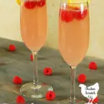 two raspberry peach mimosas in champagne flutes with lemon slices and red raspberries