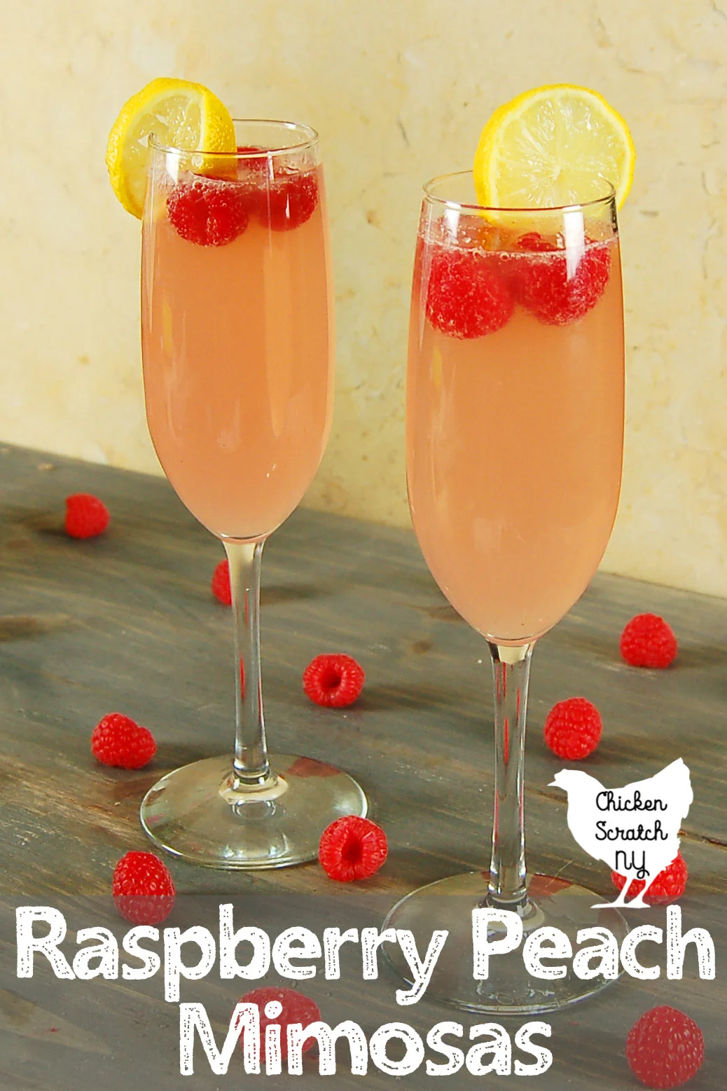 two raspberry peach mimosas in champagne flutes with lemon slices and red raspberries