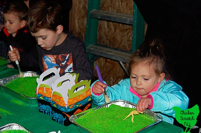 young boy and little girl using paintbrush to dig through green play sand for dinosaur bones