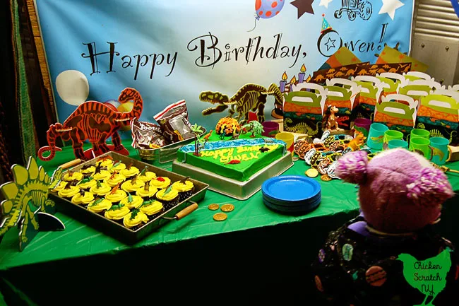 dinosaur birthday party dessert table with cupcakes, cake and party favors