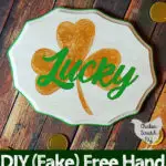 white wooden sign handpainted with a metallic gold shamrock and the work lucky in green script