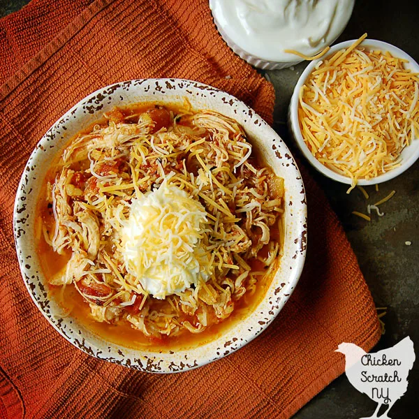 white bowl filled with instant pot chicken dinner with tomatoes and pineapple on an orange towel with two small white bowls filled with shredded cheese and greek yogurt