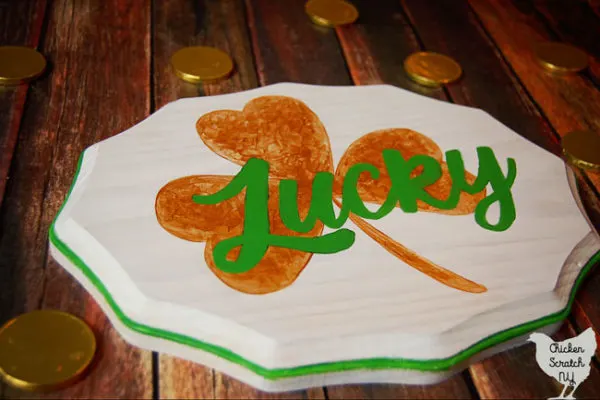 white wooden sign hand-painted with a metallic gold shamrock and the work lucky in green script