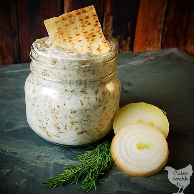 caramelized onion sip in a glass jar with fresh dill, pita chips and sliced onion on green tile
