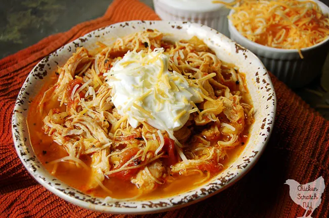 white bowl filled with instant pot chicken dinner with tomatoes and pineapple on an orange towel with two small white bowls filled with shredded cheese and greek yogurt