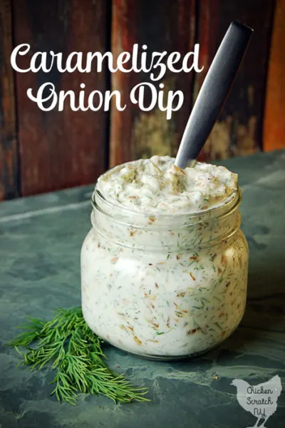 caramelized onion dip in a glass jar with fresh dill on green tile