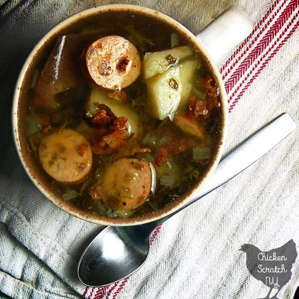 cream and blue bowl filled with red potato, chicken sausage and spinach soup topped with bacon