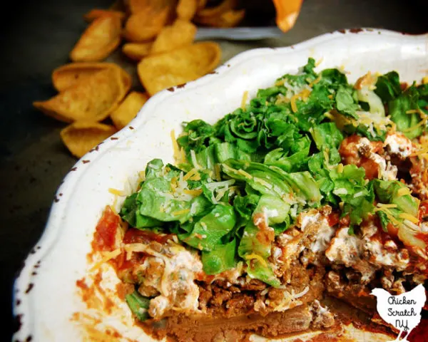 taco dip in a white bowl on a stone tile with fritos