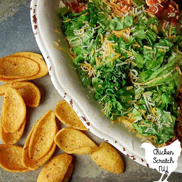 taco dip in a white bowl on a stone tile with fritos