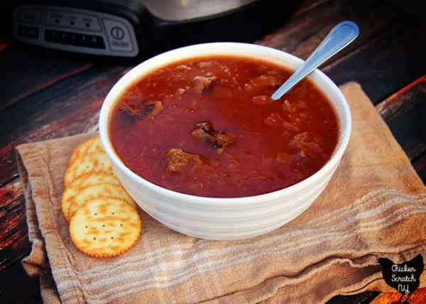 white bowl silled with tomato, sauerkraut and beef soup with ritz crackers and crock pot