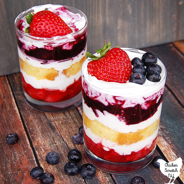 glass jar on a wooden table layered with strawberries, whipped cream, lemon pound cake and blueberries topped with fresh blueberries and a strawberry 