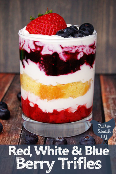 glass jar on a wooden table layered with strawberries, whipped cream, lemon pound cake and blueberries topped with fresh blueberries and a strawberry 