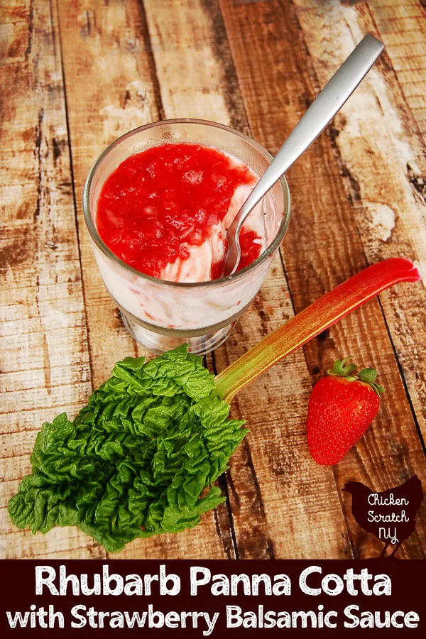 rhubarb panna cotta in a clear dish with a strawberry balsmaic sauce on a wooden board with a stalk of rhubarb and a strawberry