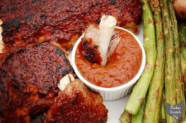 rhubarb BBQ sauce covered ribs on a white plate with a white dish filled with more BBQ sauce next to broiled asparagus