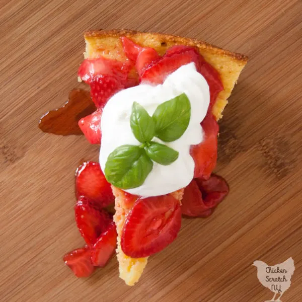 buttermilk cornbread topped with fresh strawberries and whipped cream with bail leaf on wooden cutting board