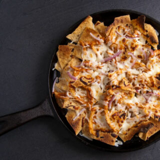 BBQ chicken nachos with red onion and mozzarella cheese on a cast iron griddle