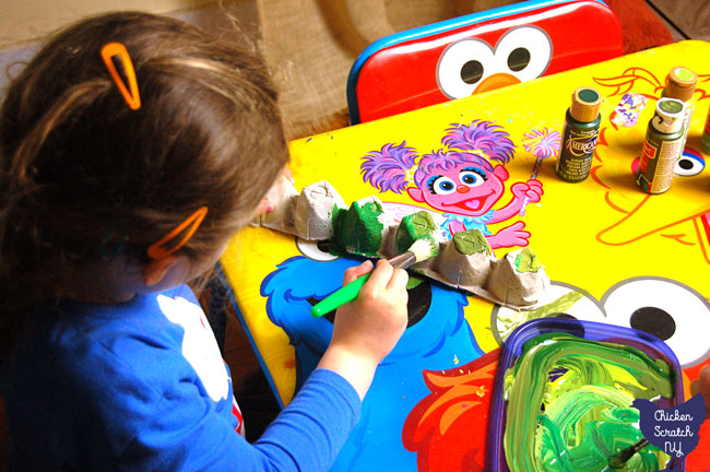 two girls painting egg cartons green at a sesame street table