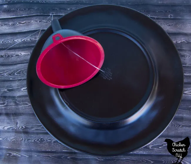 plastic plate painted black with a hole drilled in the center with a red funnel spray painted black stung together with fishing line 