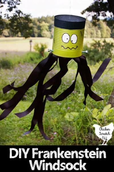 tin can turned into DIY Frankenstein Windsock with paint, screws and ribbon hanging in a tree with the black ribbon streamers blowing in the breeze