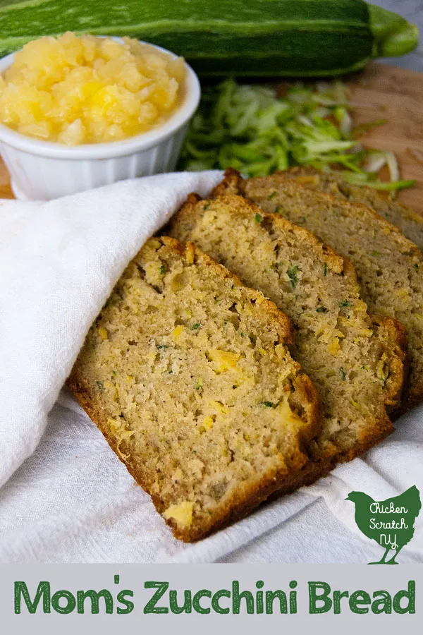 homemade sliced pineapple zucchini bread wrapped in a white tea towel in front of a cutting board with shredded zucchini and crushed pineapple in a white dish