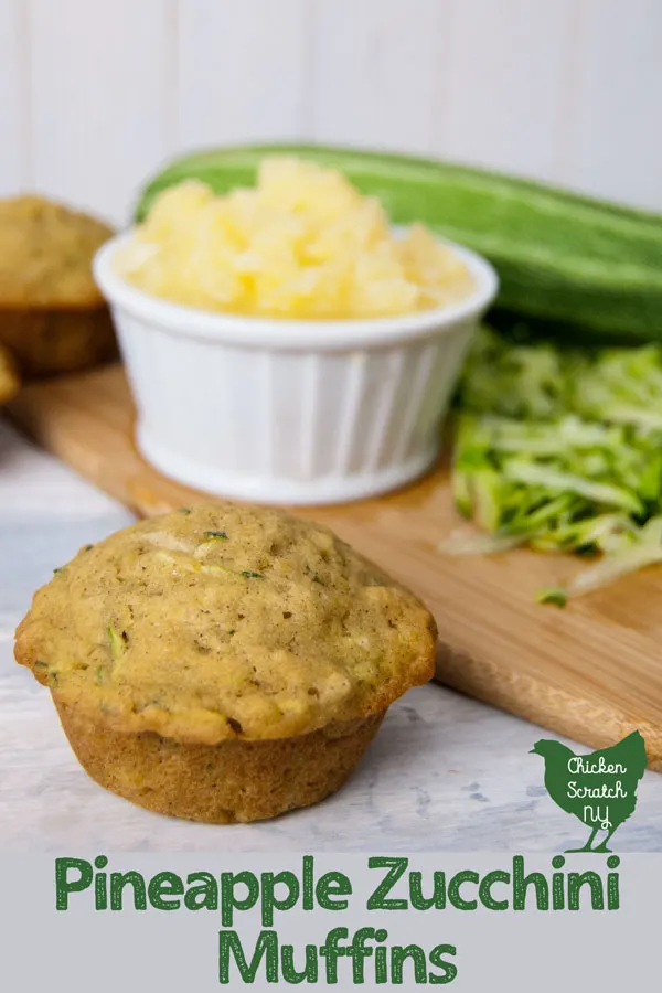 homemade pineapple zucchini muffins in front of a cutting board with shredded zucchini, a whole zucchini and crushed pineapple in a white dish