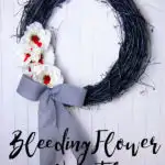 black grapevine wreath with bleeding white flowers and a grey bow on a white wooden background