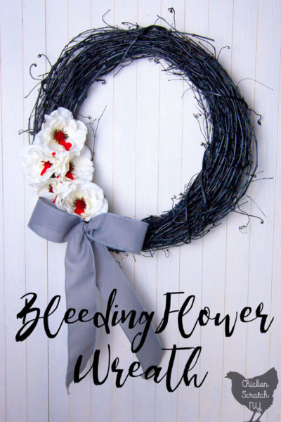 black grapevine wreath with bleeding white flowers and a grey bow on a white wooden background