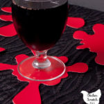 glass of red juice on a red vinyl hand made coaster shaped like a blood splatter