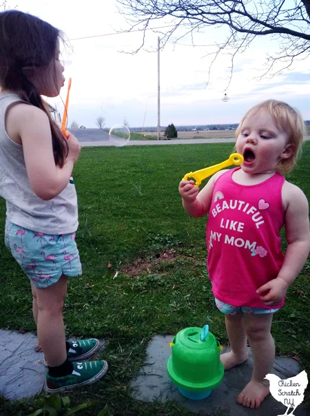 two little girls in summer clothes blowing bubbles from an untippable bubble solution holder