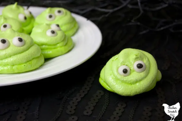 white plate full of lime green meringue cookies with eyes that look like Blobby from Hotel Transylvania on a black surface