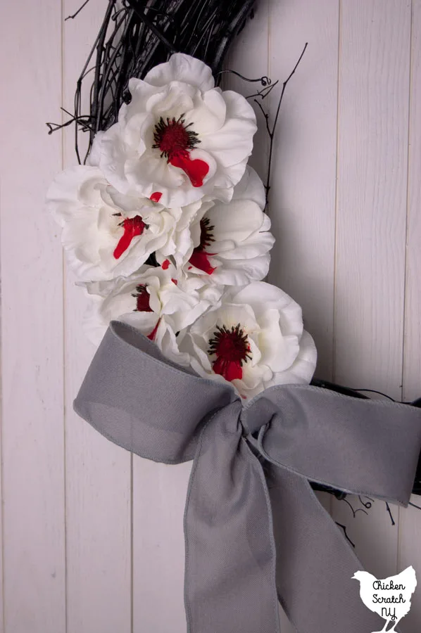 black grapevine wreath with bleeding white flowers and a grey bow on a white wooden background