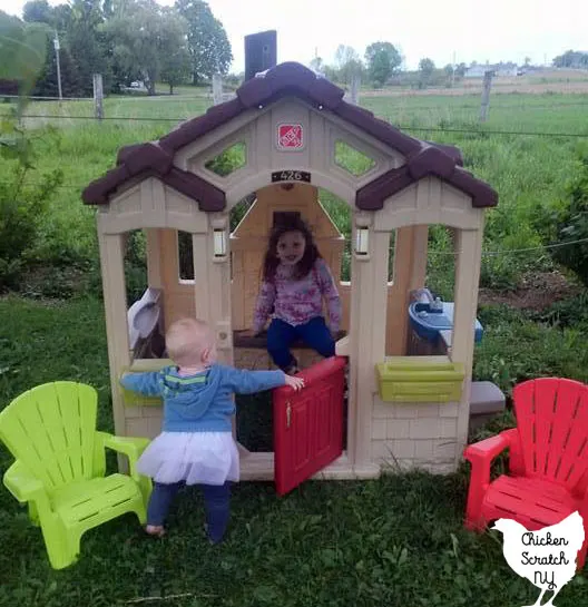 two little girls in a plastic plastic playhouse with little plastic Adirondack chairs