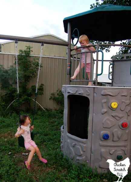 two girls in pink shirts and shorts playing on a large back yard metal swing set
