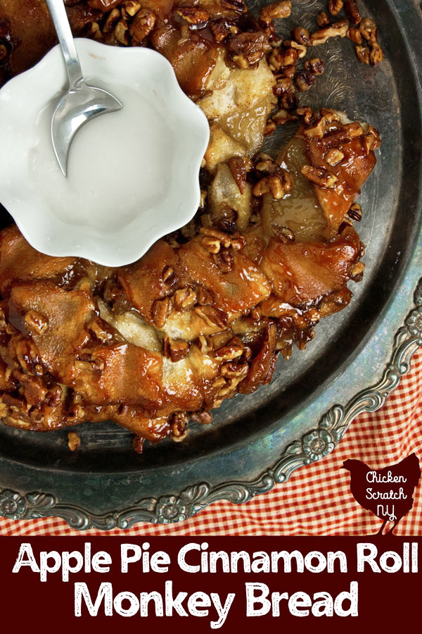 top view of silver plate with ring of apple pie cinnamon roll monkey bread with small white fluted bowl full of icing with silver spoon