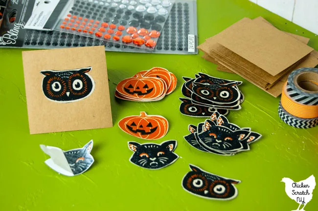 half assembled Halloween banner with kraft paper not card with fabric cat face attached next to piles of cut out Halloween fabric shapes 
