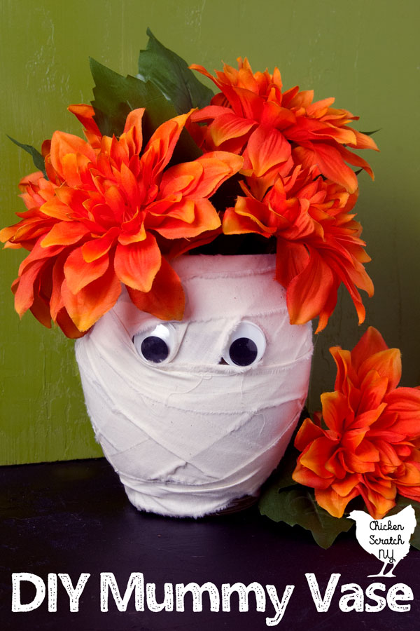 mummy vase made out of a dollar store vase covered in strips of muslin with two googley eyes filled with fake orange flowers