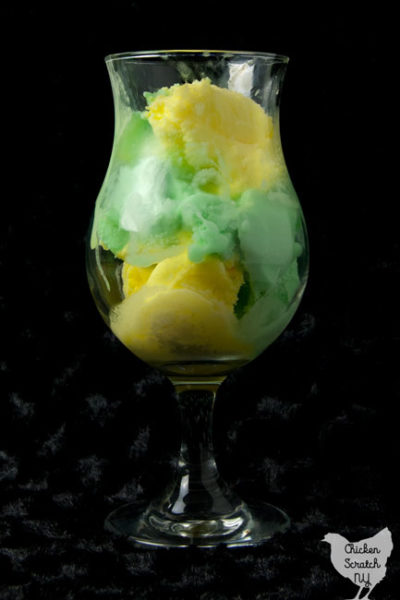 clear ice cream glass filled with lemon and lime sherbet against a black background