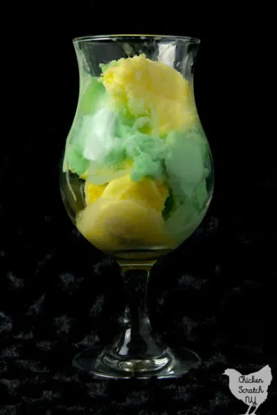 clear ice cream glass filled with lemon and lime sherbet against a black background