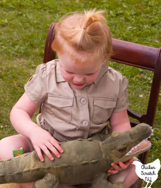 young blonde girl in a khaki saffri shirt hugging a stuffed crocodile dressed like Steve Irwin