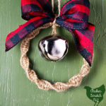 Macramé wreath ornament made with twine, silver bell and and buffalo check ribbon